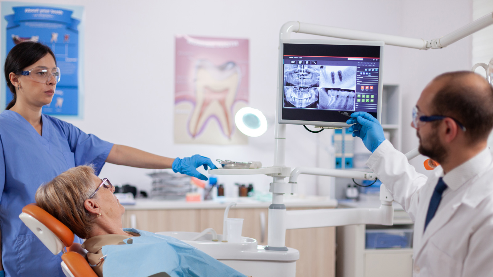 Dentistul examinează radiografia și explică diagnosticul unei femei în vârstă.