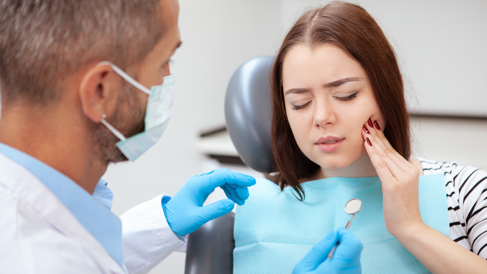 Femeie tânără cu durere de dinți, stând în scaunul stomatologic din clinică.